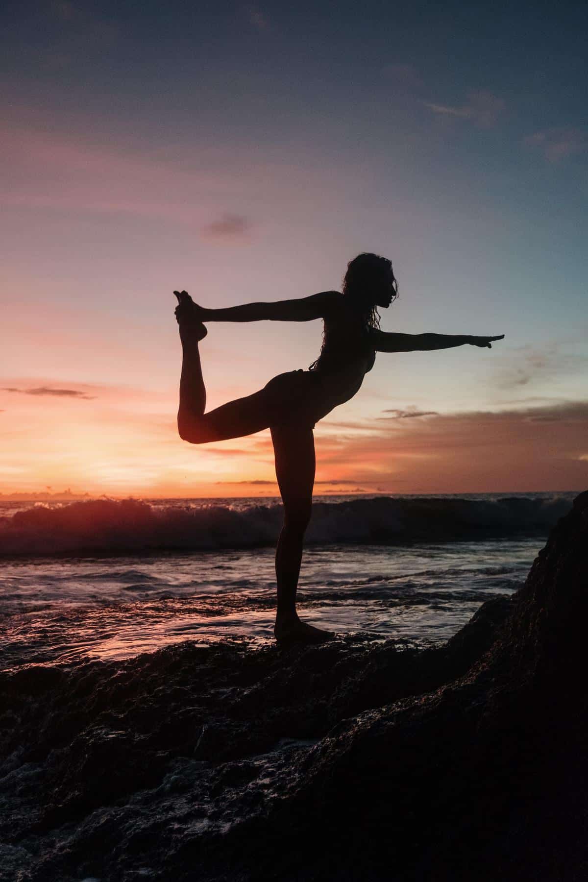 Illustration of a person performing a yoga pose on a mountain peak with a sunset background, representing balance and flexibility in adventure travel.